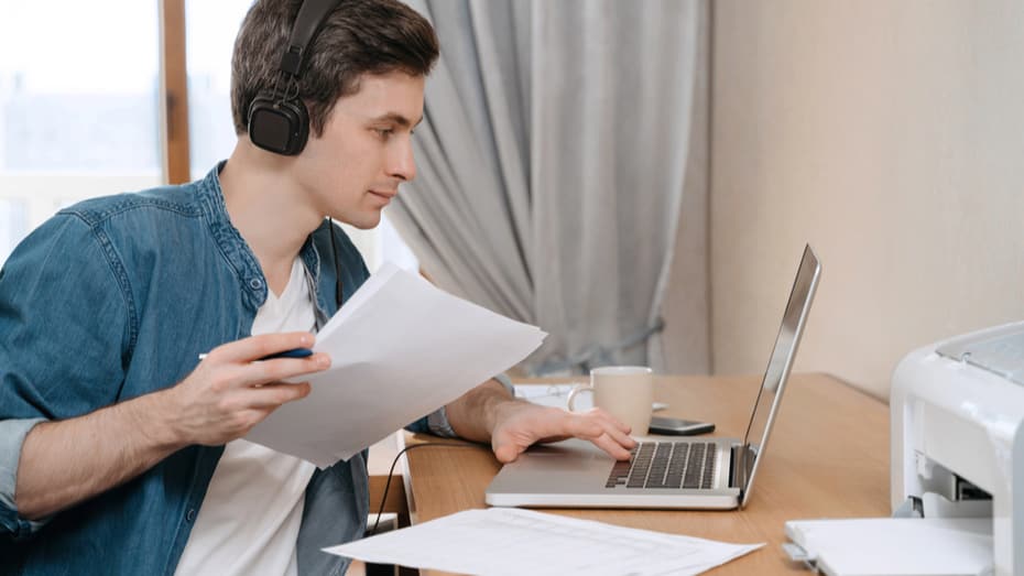 man working from home on laptop, printing documents from printer